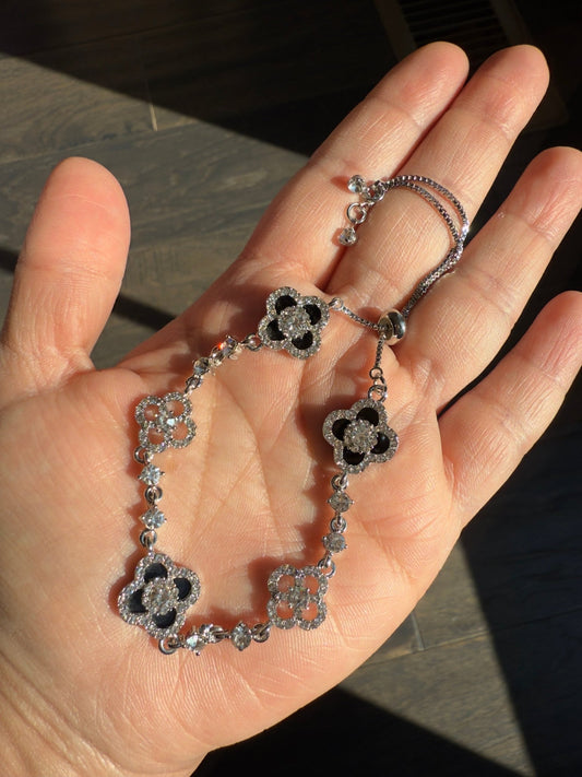 Silver bracelet with floral designs held in a hand against a dark background